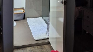 Een kamer met een bed, nachtkastje, kapstok, spiegel en een deur naar een badkamer met een handdoek aan de muur.