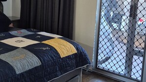 Een slaapkamer met een bed, een raam met gordijnen, een deur met hor en uitzicht op buiten.