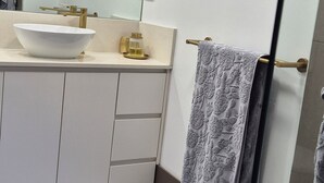 Een moderne badkamer met een grote spiegel, een wastafel, een handdoekhouder en een zacht, wit kleed.