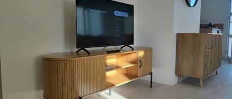 Una sala moderna con un televisor de pantalla plana montado en un mueble de madera, un aparador con cajones y un espejo en la pared.