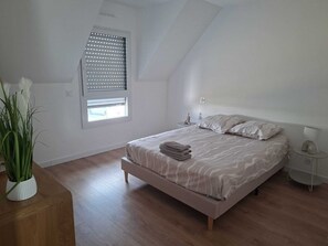 Un dormitori amb sostre inclinat, un llit amb col·locador estampat, una taula de nit amb una làmpada i una finestra amb persianes.