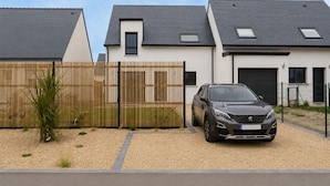 A modern two-story house with a car parked in the driveway, a wooden fence, and a gravel path. - Quiet house just 5 minutes from the beaches with direct access to the bike path  (Clohars-Carnoët)