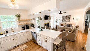 A modern kitchen with white cabinetry, a central island, and a dining area with a sofa. - The Willow-A Seabrook Coastal Retreat Near Beaufort & Hunting Island (Seabrook)