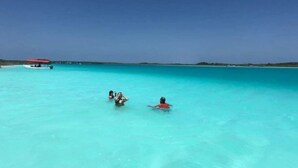 A clear turquoise sea with a boat in the distance and two people swimming. - CAMPING CABIN 5 (Bacalar)