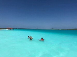 Ein klares, türkisfarbenes Meer mit einem Schiff in der Ferne und zwei schwimmenden Personen.