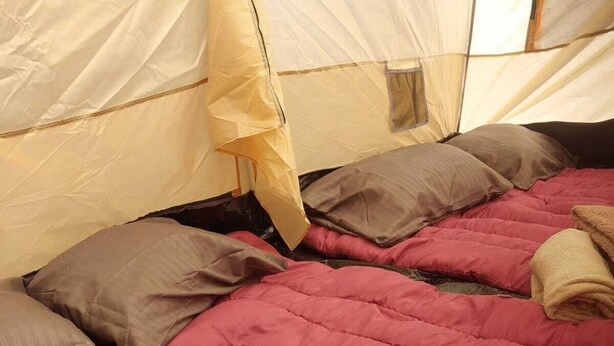 A tent with a red quilted bedspread, a brown pillow, and a beige blanket. - CAMPING CABIN 5 (Bacalar)