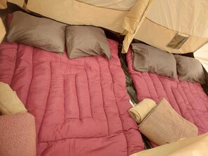 Un lit avec une couette rose et des oreillers beige, une structure en forme de tente au-dessus, et une fenêtre.