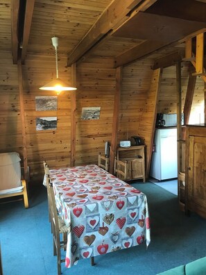 Ein gemütliches Blockhaus mit Holzvertäfelung, einem Esstisch mit Tischdecke mit Herzmuster, einem Bett und einer Küchenzeile.