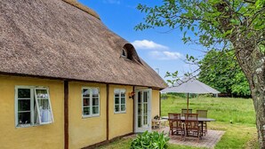 Una casa con techo de paja, un patio y mobiliario exterior.
