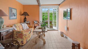 Una habitación acogedora con un sofá, una mesa, una lámpara y una silla. Se ve vegetación por la ventana.