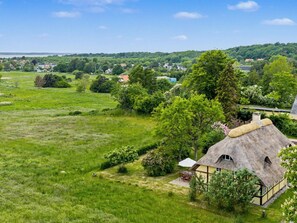 A rural landscape with a thatched-roof house surrounded by greenery and a distant view of a body of water. - "Sida" - 1.3km from the sea by Interhome (Tranekær)