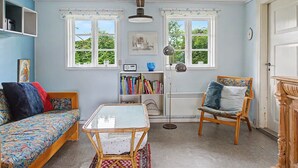 Una habitación con un sofá, una silla, una mesa, una estantería y dos ventanas.