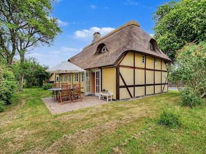 Una casa tradicional de entramado con techo de paja, un patio con mobiliario exterior y un jardín bien cuidado.