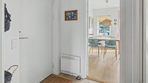 Un couloir mène à une salle à manger équipée de chaises et d’une table, ainsi qu’un radiateur et une porte sur laquelle est accroché un sac.