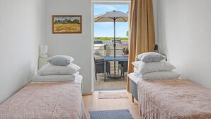 Une chambre avec deux lits, un tableau, une table avec des chaises et une vue sur l’extérieur.