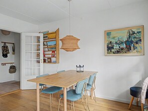A dining area with a wooden table and blue chairs, a hanging light fixture, a bookshelf, and a painting on the wall. - "Riku" - 15m from the sea by Interhome (Rudkøbing)