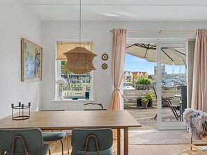 A dining area with a wooden table and chairs, a hanging light fixture, a window with blinds, and a view of a marina through a glass door. - "Riku" - 15m from the sea by Interhome (Rudkøbing)