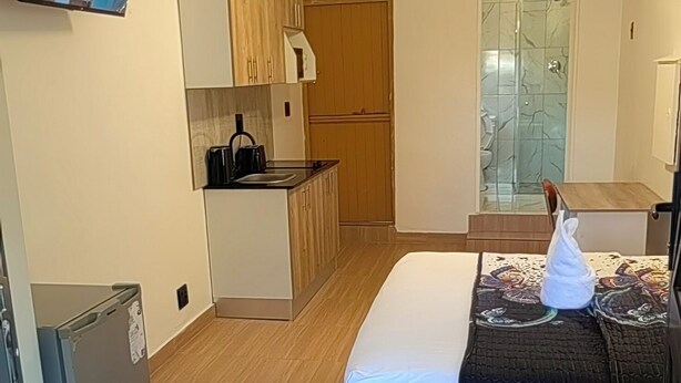 Ein gemütlicher Raum mit Bett, einer kleinen Küchenzeile, einer Dusche und einem an der Wand befestigten Fernseher.