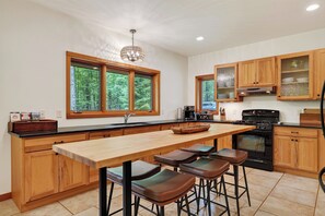 Cocina con isla de madera, taburetes de bar, estufa y ventana con vistas a árboles.