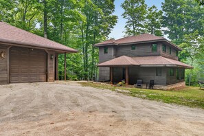 A two-story house with a garage, a covered porch, and a driveway leading to the house. - Jacksonport Woodland Hearth Retreat - Near Lake Michigan (Sturgeon Bay)