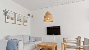 Un salon moderne avec un canapé, une table en bois, un téléviseur fixé au mur et un luminaire suspendu.