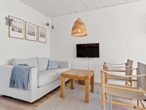 Ein modernes Wohnzimmer mit einer Couch, einem Holztisch, einem an der Wand montierten Fernseher und einer Pendelleuchte.