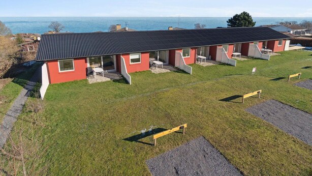 Une rangée de bâtiments rouges surmontés d’un toit noir, chacun doté d’une terrasse et offrant une vue sur la mer.