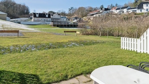 Un espace extérieur verdoyant avec un banc, une clôture blanche et, au fond, un bâtiment doté d’un toit en pente.