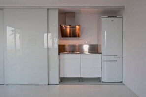 A compact kitchen with a built-in stove, a stainless steel range hood, and a white refrigerator. - Romantic Beachfront Suite with Ocean Views (El Campello)
