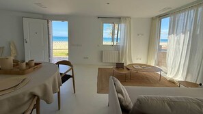 A room with a dining table, chairs, a sofa, a small round table, and a view of the beach. - Romantic Beachfront Suite with Ocean Views (El Campello)