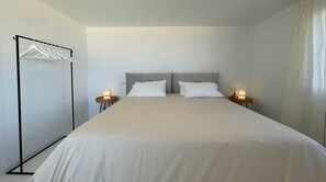 A hotel room with a bed, two bedside tables, a wall-mounted drying rack, and a curtain. - Romantic Beachfront Suite with Ocean Views (El Campello)