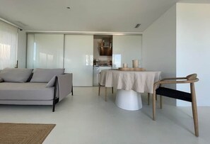 Una sala de estar moderna con un sofá, una mesa de comedor con sillas y una zona de cocina al fondo.