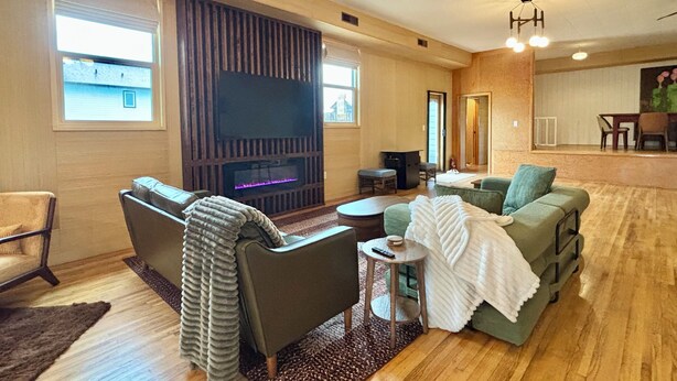A living room with a fireplace, a sofa, a green couch, a small table, and a TV. - Historic Hall Retreat | 3BR Mountain Getaway (Lundbreck)