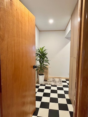 Un couloir avec un sol à carreaux, une porte en bois, une plante en pot et un radiateur.