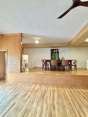Une pièce spacieuse avec un plancher en bois, une table à manger avec des chaises et un ventilateur de plafond.