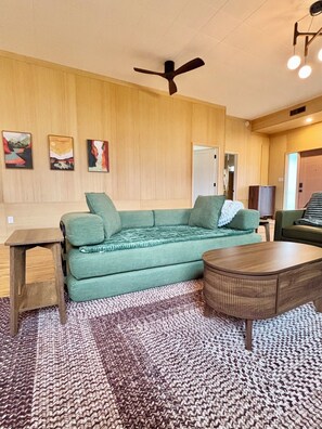 Un salon avec un canapé vert, une table basse en bois, un lampadaire et un ventilateur de plafond.