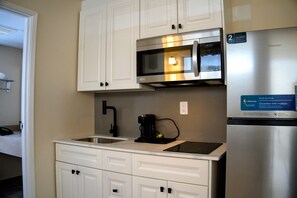 Una cocina compacta con armarios blancos, un microondas de acero inoxidable, una cafetera y un refrigerador.