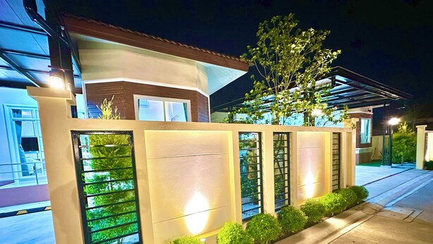 Um edifício moderno com entrada protegida por portão, caminho bem iluminado e uma árvore.