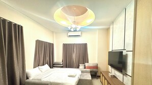 Quarto de hotel moderno com cama, televisão, luminária no teto e cortinas.
