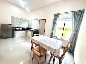 A dining area with a table, chairs, a refrigerator, a kitchen area, and a window with curtains. - Rakraekpobresortsattahip (Sattahip)