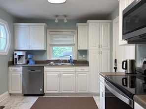 Una cocina con gabinetes blancos, lavavajillas de acero inoxidable, cafetera y microondas.
