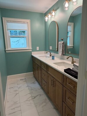 Un bagno con pareti color verde acqua, un mobile vanità bianco, due lavandini, uno specchio grande e una finestra.