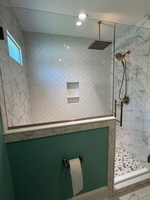 A bathroom with a herringbone tile pattern, a shower with a handheld showerhead, and a toilet paper holder. - Charming Haymount 2BR/2BA Home & Walkable Restaurants and Bars (Fayetteville)