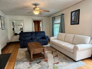 A living room with a ceiling fan, two sofas, a coffee table, and a rug. - Charming Haymount 2BR/2BA Home & Walkable Restaurants and Bars (Fayetteville)
