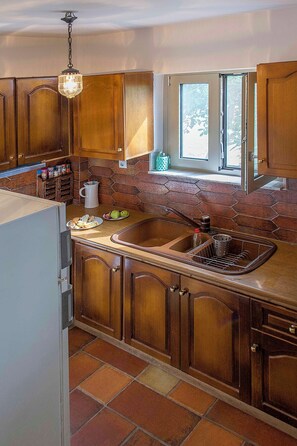 A kitchen with wooden cabinets, a stone backsplash, a window, and a hanging light fixture. - Traditional sea front villa, close to reasturants & cafes
With garden & sea view (Kalamata)