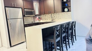 A modern kitchen with stainless steel appliances, a central island with bar stools, dark wood cabinets, and a decorative backsplash. - My Paradise: Tropical, 3-star, beach, sand—everything at your fingertips (Carolina Puerto Rico)