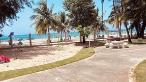 Ein Park am Strand mit einem Betonweg, Bänken und einem eingezäunten Bereich.