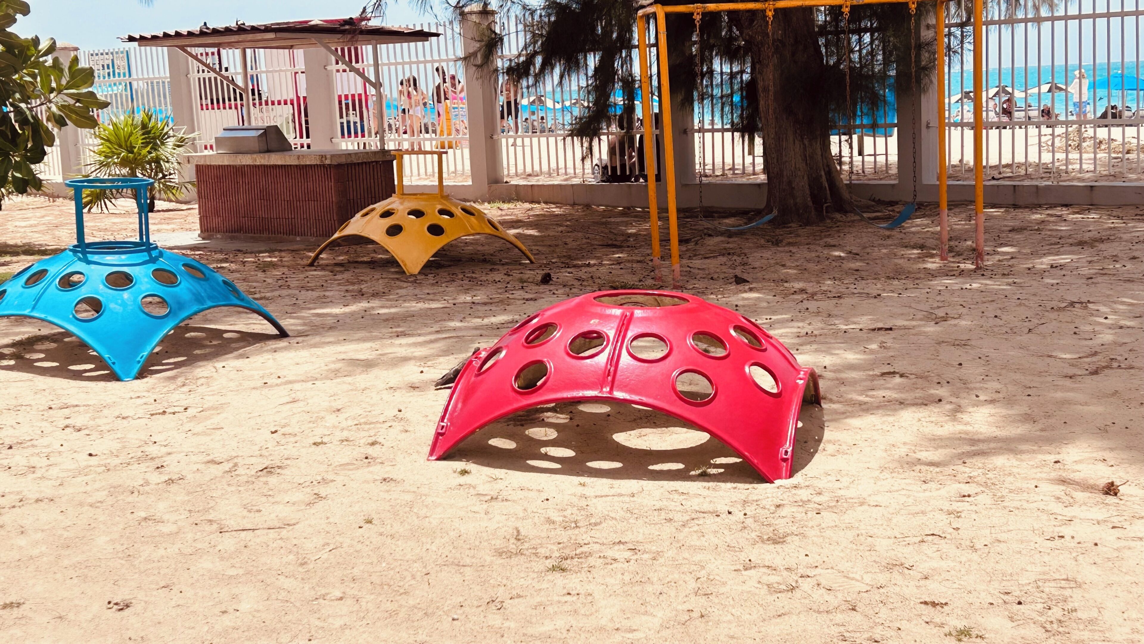 A sandy playground with three colorful play structures.