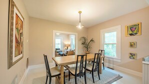 A dining area with a wooden table and chairs, a hanging light fixture, and artwork on the walls.