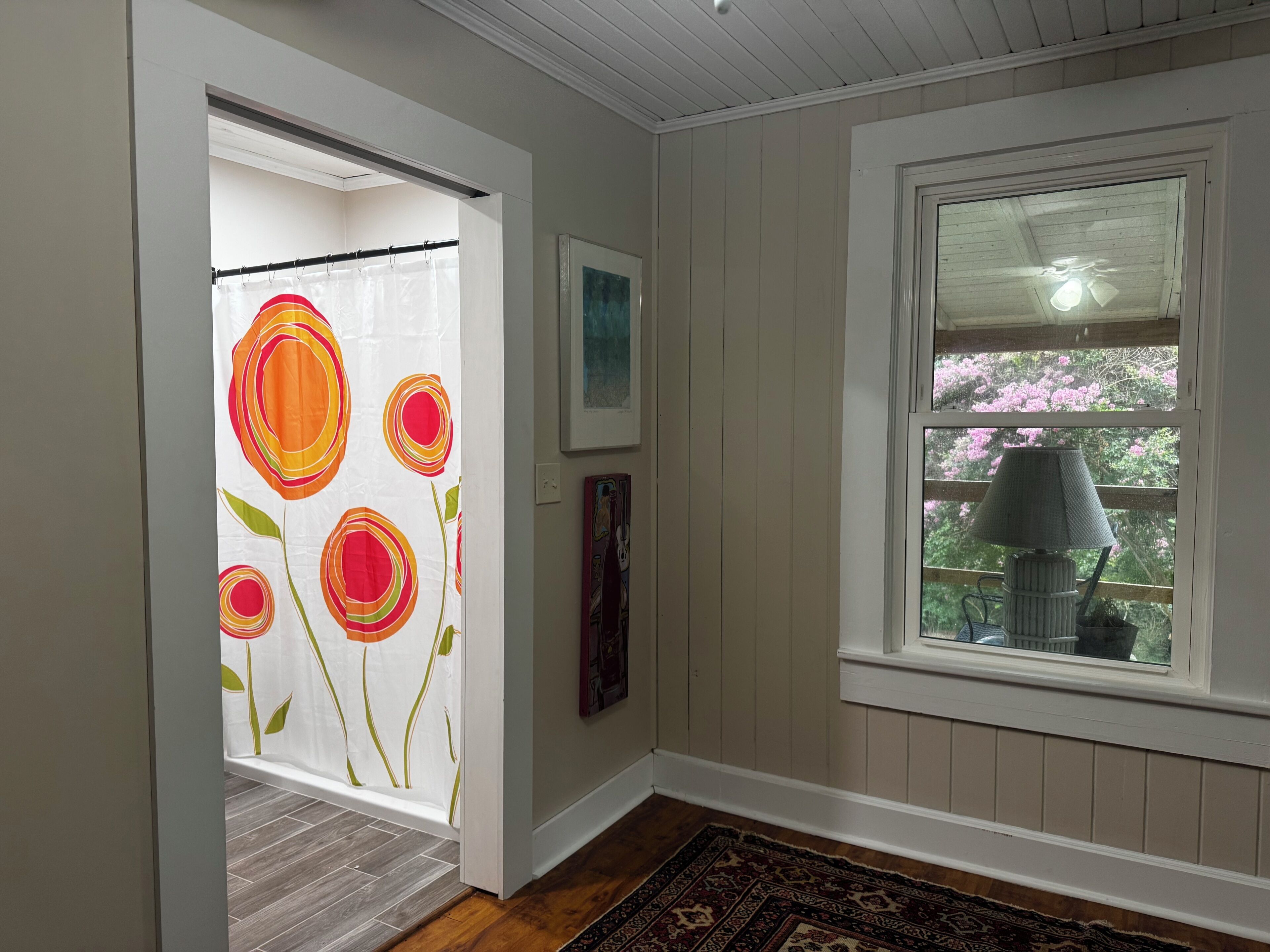 A room with a window, a door with a floral curtain, and a rug on the floor.